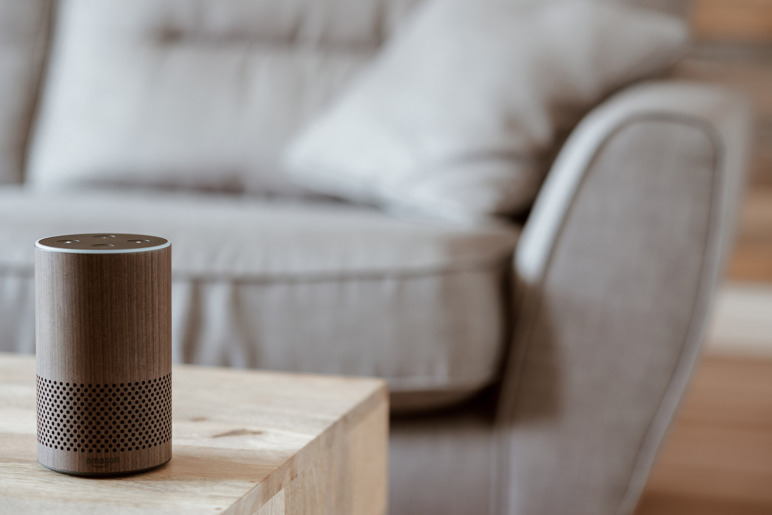 A smart speaker sits on a coffee table with a couch in view in the background