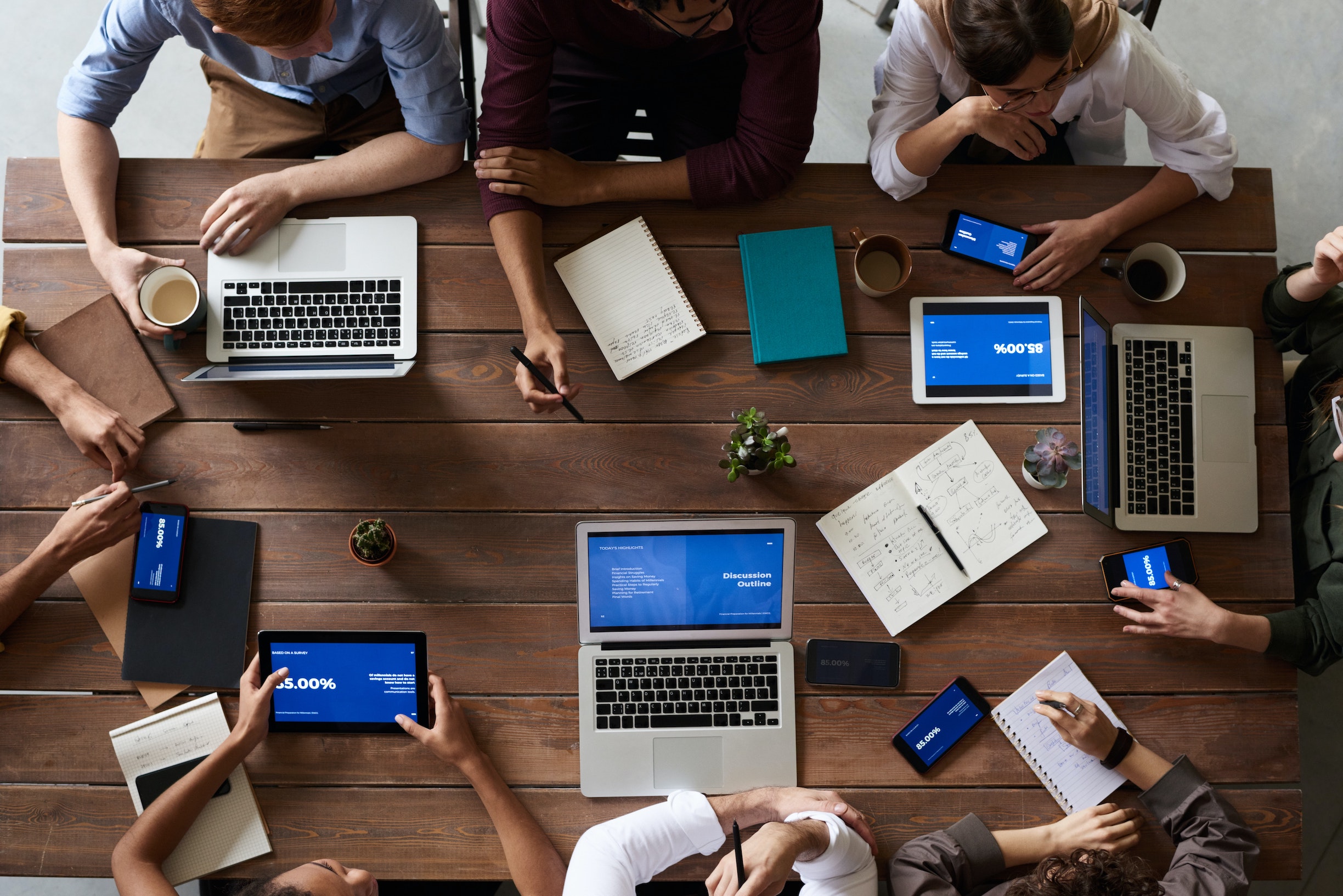 Overhead view of people working around a table with laptops, tablets and notebooks