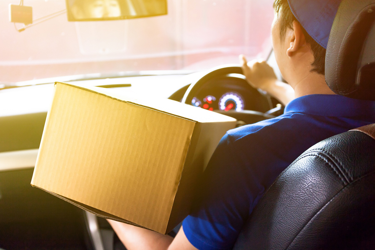 A delivery driver holds a box while steering a vehicle