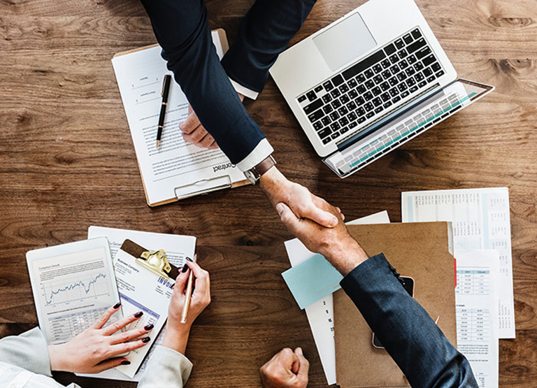 Two men shake hands over a pile of papers