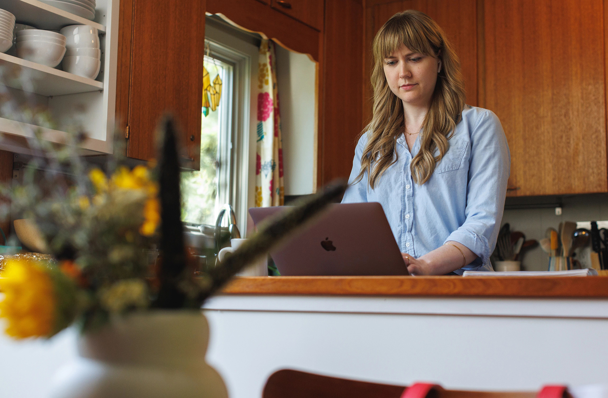 A woman in her kitchen uses a laptop positioned on a counter