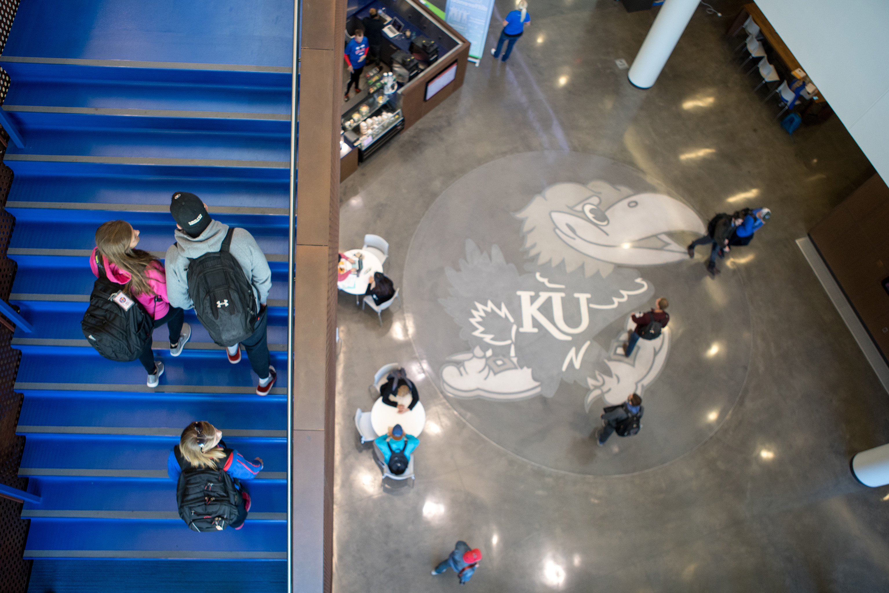 Overhead shot of students walking up a staircase in Capitol Federal Hall with a Jayhawk concrete design in the background.