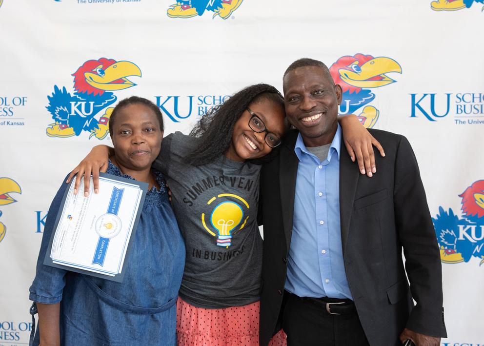 A 2022 SVB participant wraps her arms around her parents to take a photo with her SVB certificate