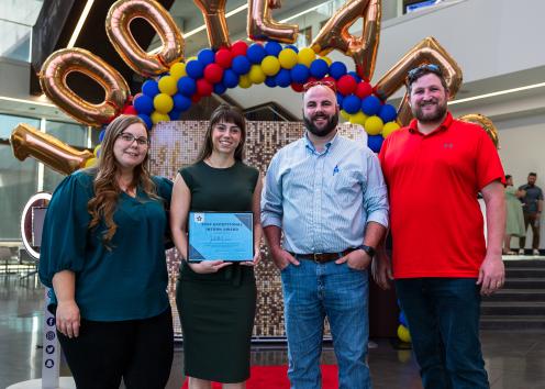 Isabelle Larsen holds the 2024 Exceptional Intern Award from the EY Business Professional Development Program with three people standing next to her. 